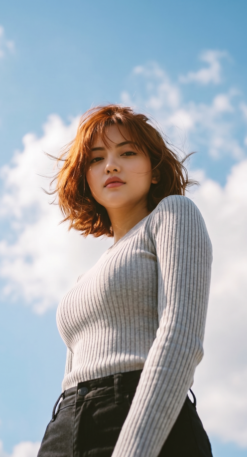 A low-angle, worms-eye view photograph of a young East Asian woman looking down at the camera with a confident, serene expression
